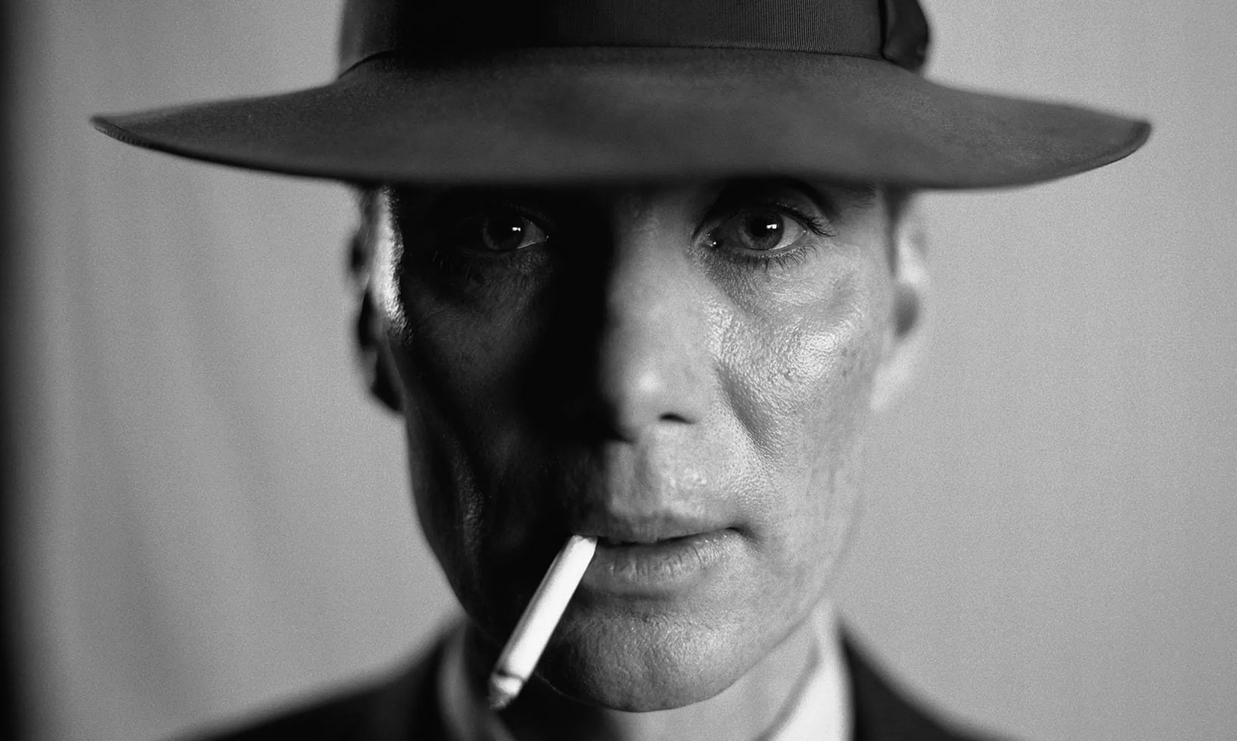 Black and white close-up of a famous person on screen wearing a hat and smoking a cigarette, posing seriously.