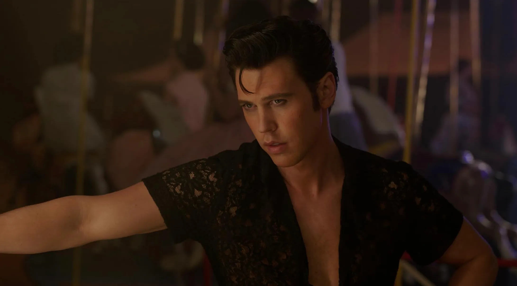 Austin Butler portraying a famous character in a movie scene, wearing a black lace shirt and looking intense.