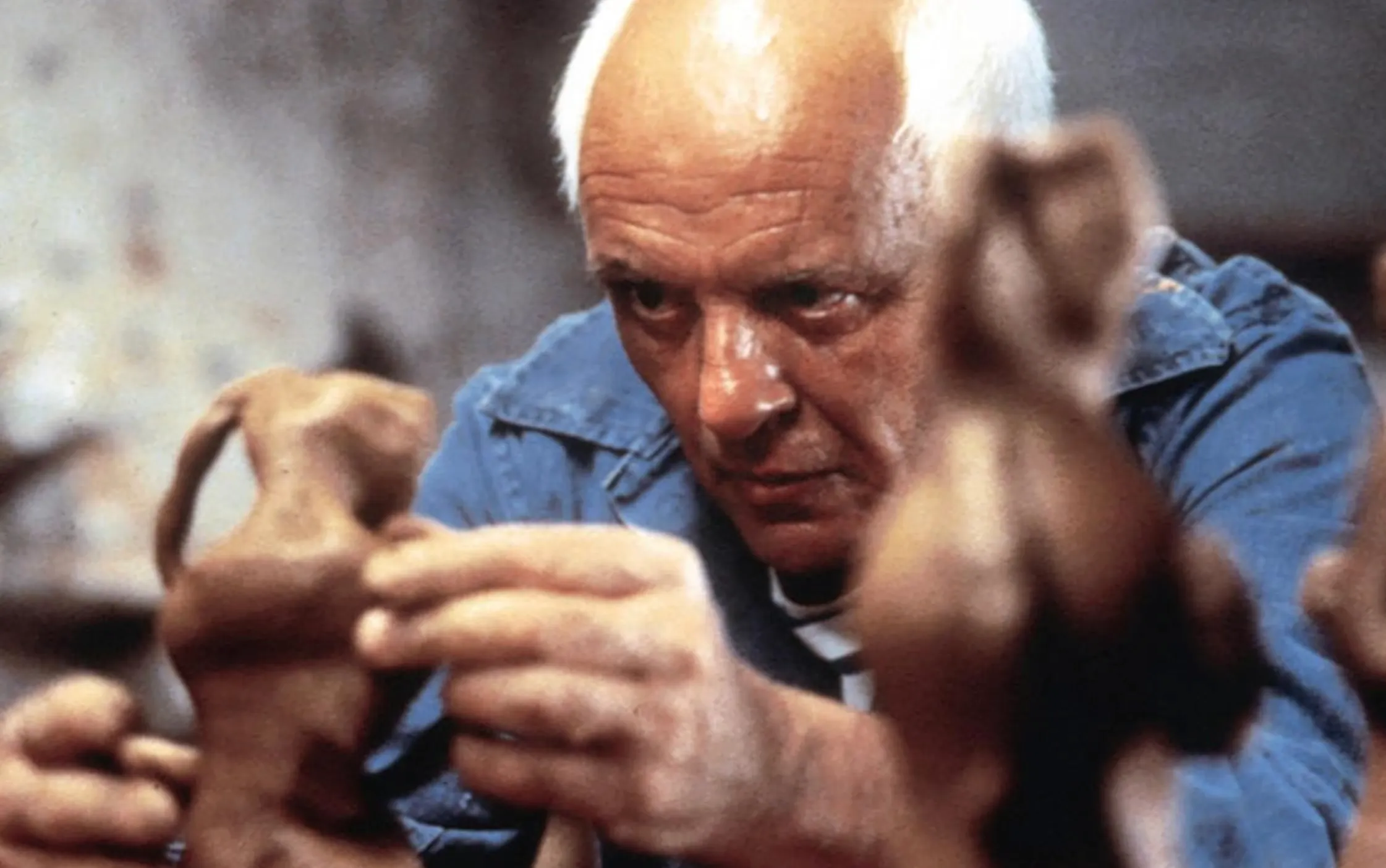 Sir Anthony Hopkins portraying a character intensely studying clay figures in a movie scene.