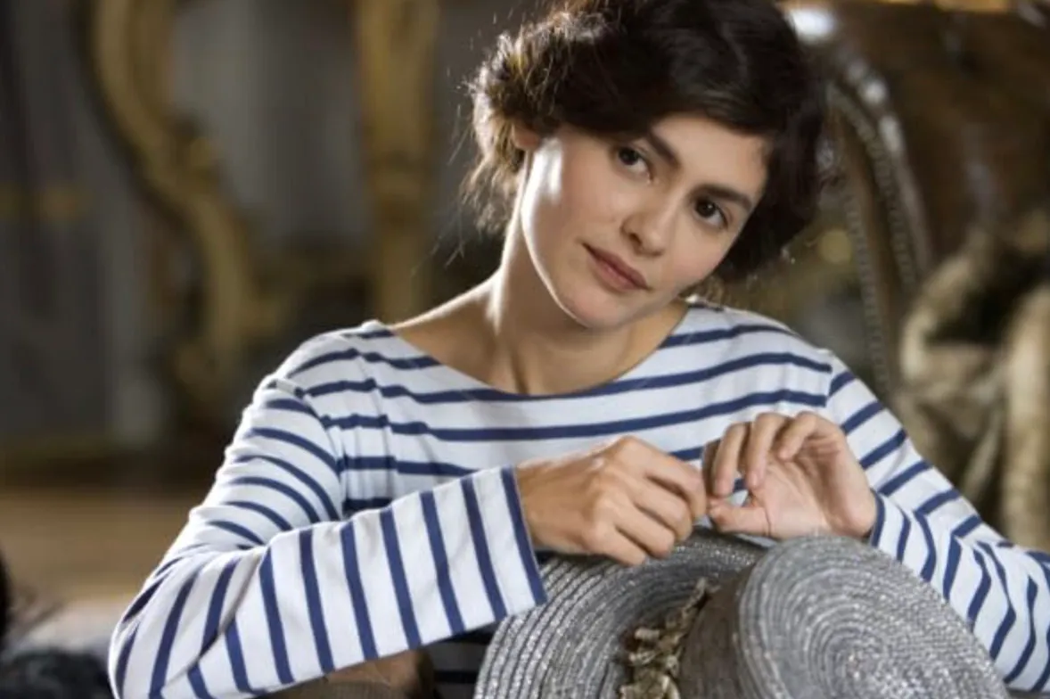 Audrey Tautou portraying a fashion icon in a 2009 film, wearing a striped shirt and holding a hat.