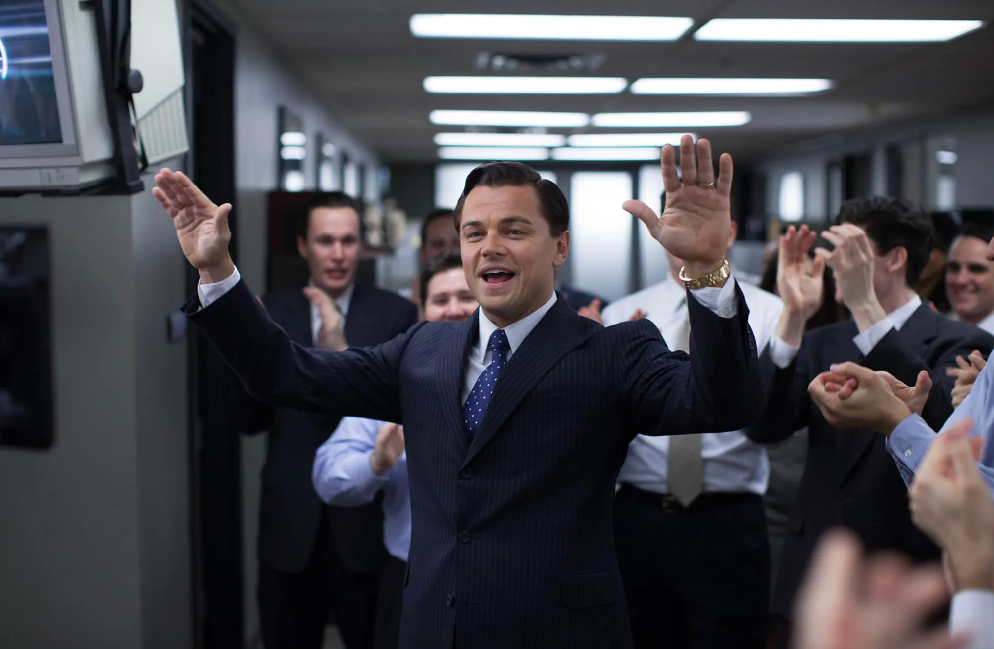 Leonardo DiCaprio impersonating a stockbroker in The Wolf of Wall Street celebrating with colleagues in an office.