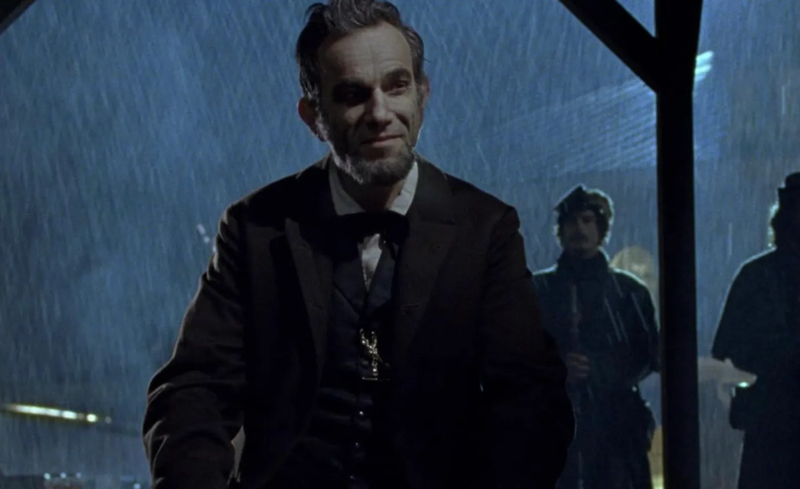 Daniel Day-Lewis portraying Abraham Lincoln in a rainy nighttime scene from the film Lincoln, dressed in period attire.