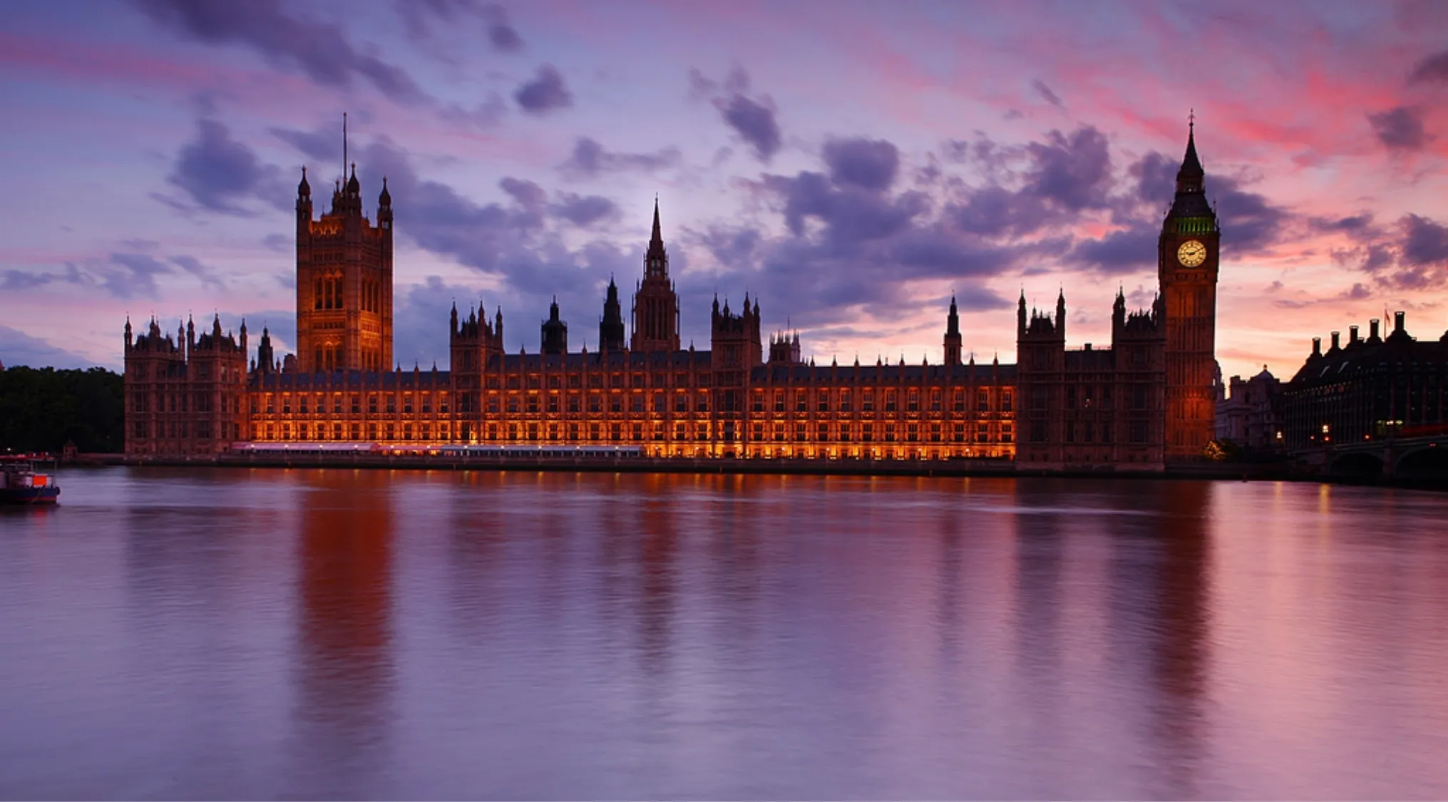 The illuminated UK Parliament building at dusk reflecting on the River Thames, related to UK citizenship test questions.