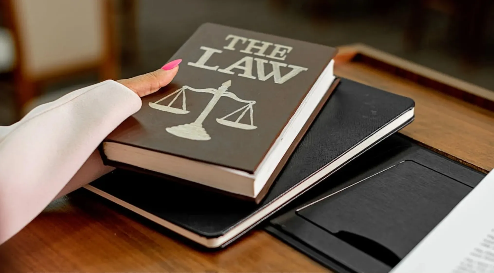 Hand holding a book titled The Law with a scales of justice symbol, related to UK citizenship test civil law questions.