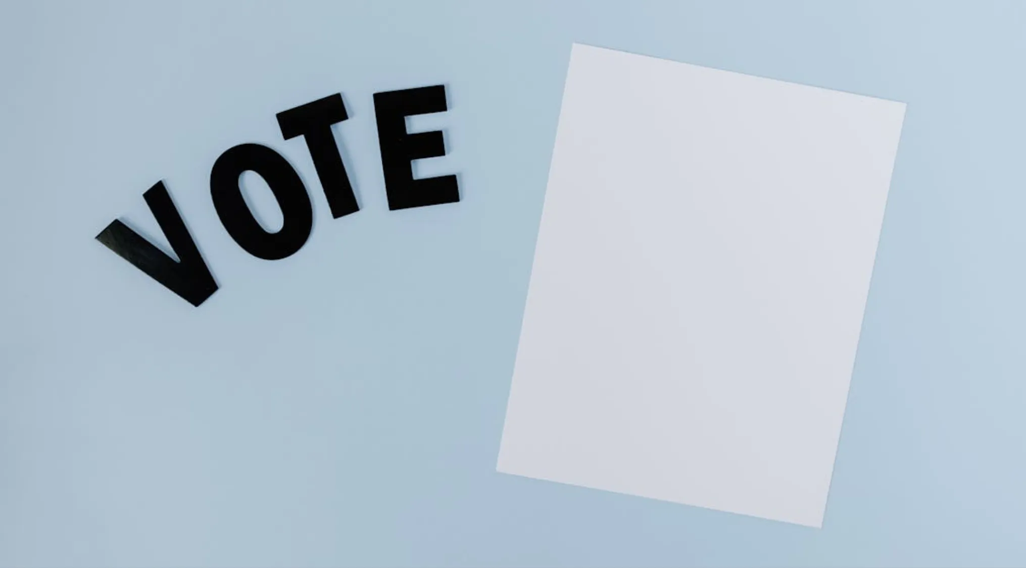 Black letters spelling vote next to blank white paper on blue background representing UK citizenship test questions.