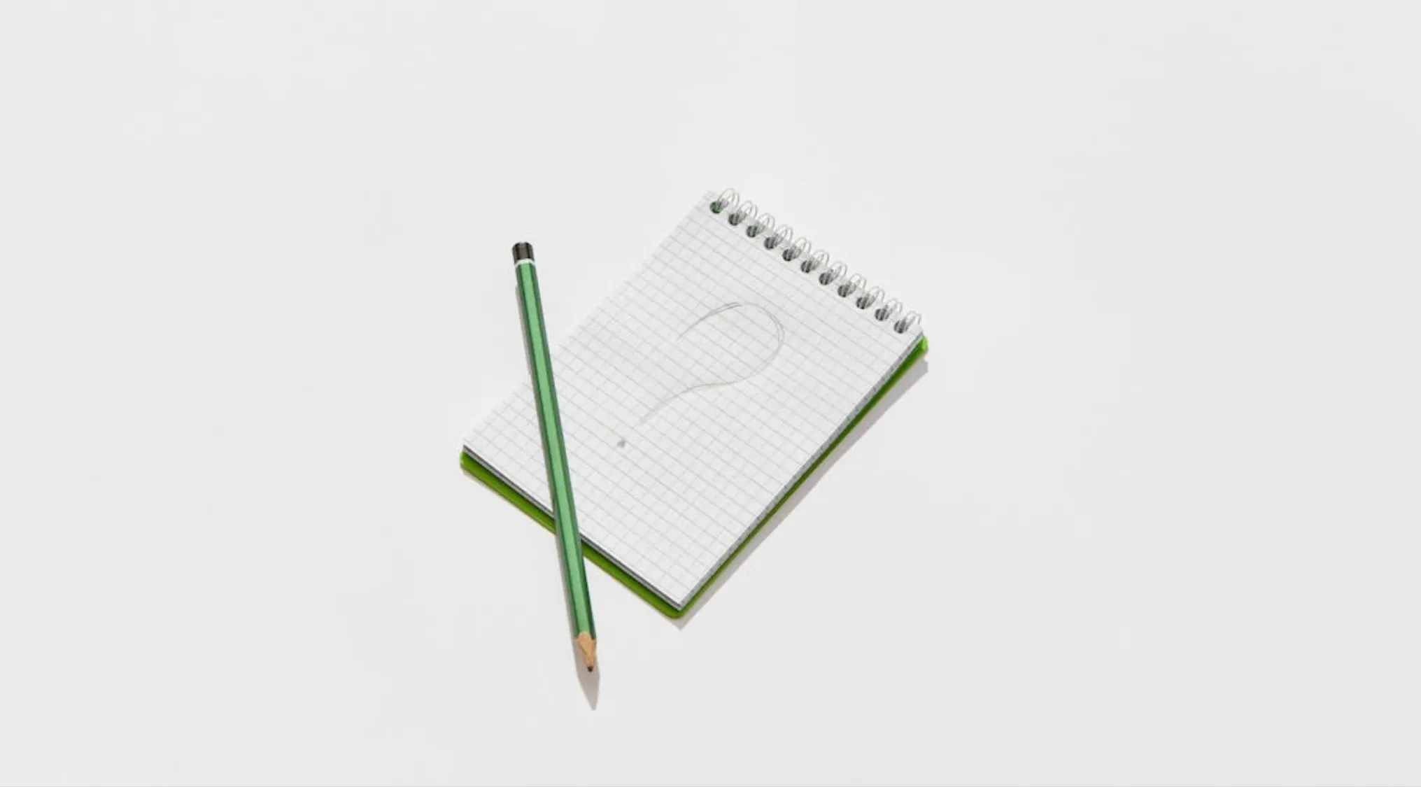 Green pencil resting on a small checkered notebook with a question mark, symbolizing UK citizenship test questions.