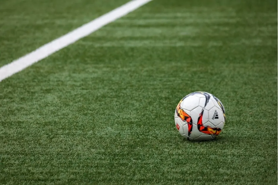 Football on green artificial turf near a white line marking on a grassy sports field.