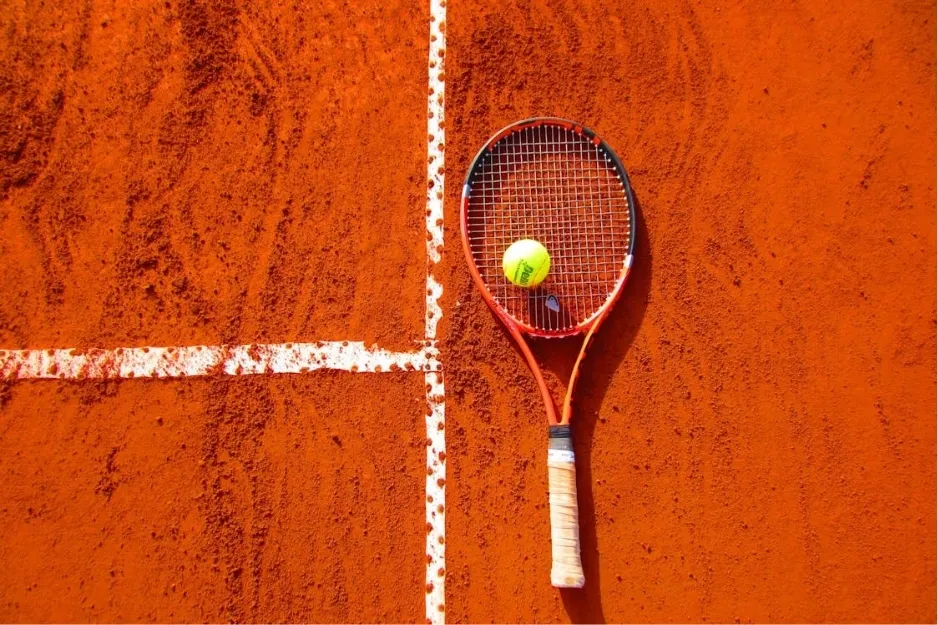 Tennis racket and ball resting on a clay court near white boundary lines, highlighting tennis equipment and surface.