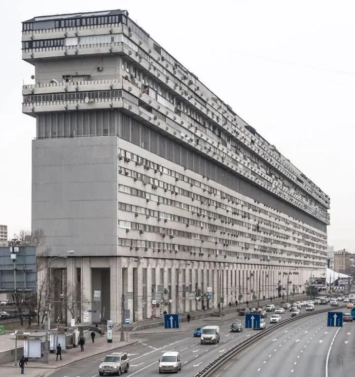Massive gray brutalist apartment building along a busy urban highway depicting dystopian urban hell environment.