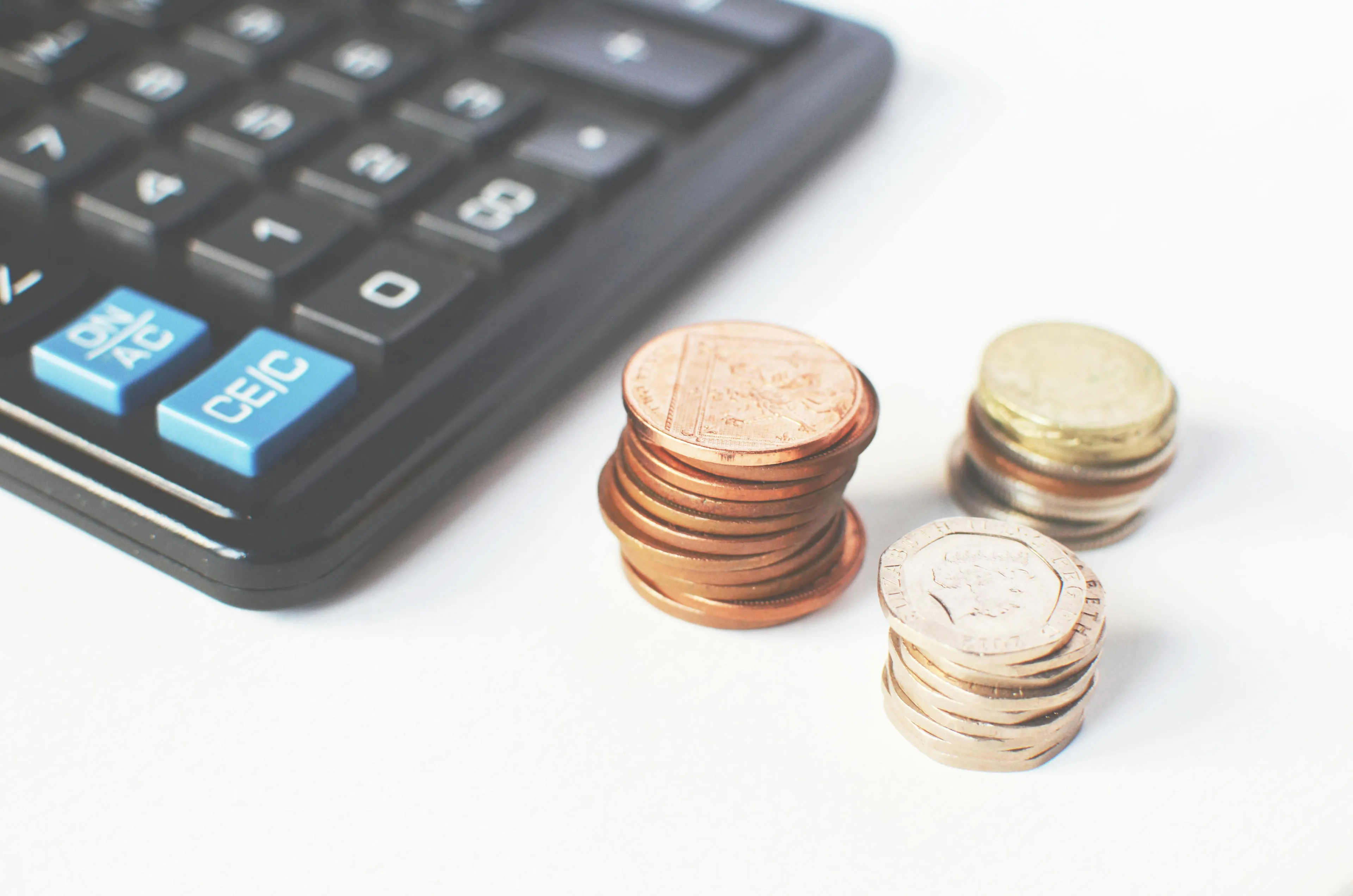 Calculator next to stacks of coins representing economics and the price principle of reduced demand with higher cost.