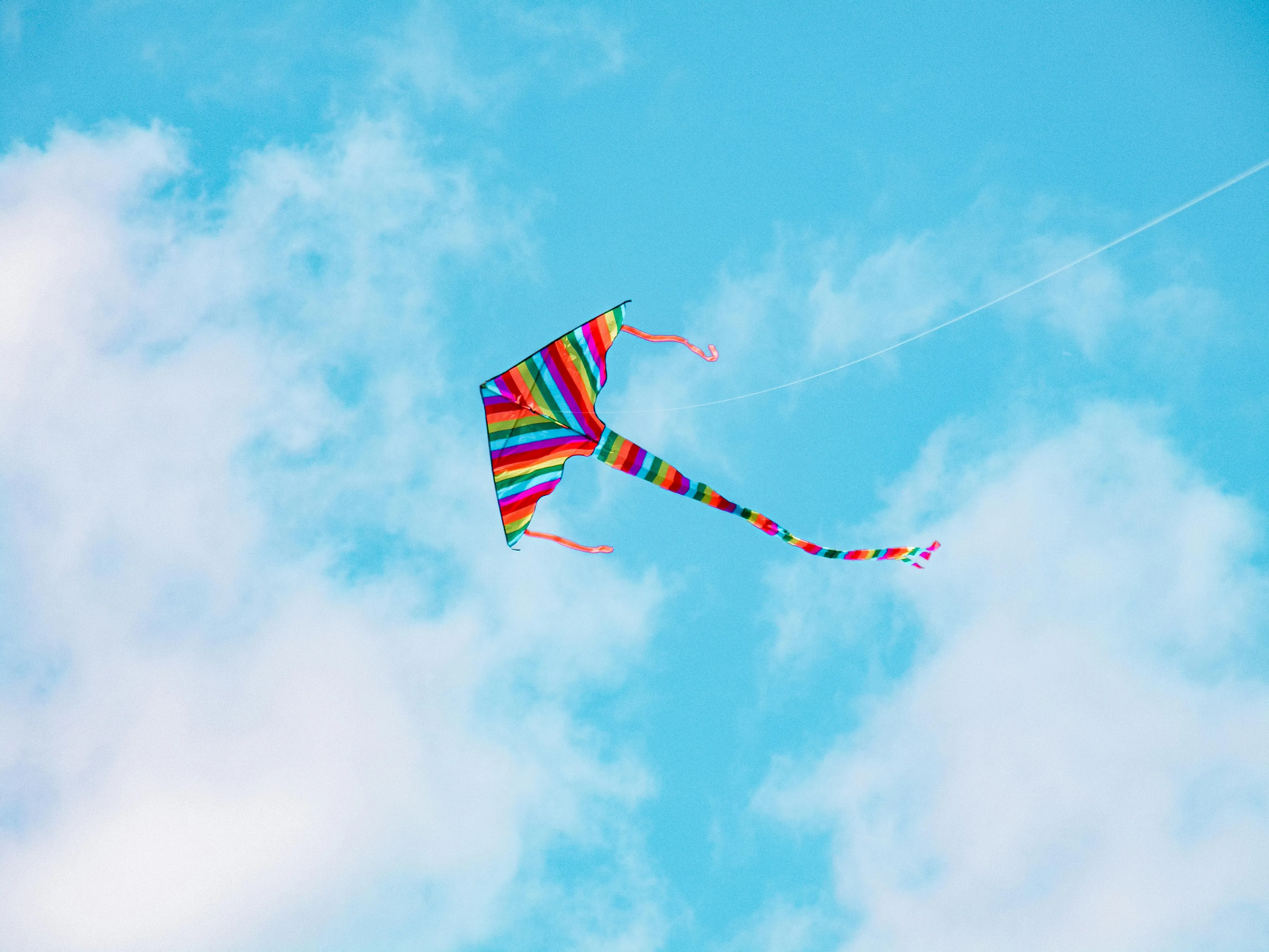 Colorful striped kite flying in a clear blue sky illustrating science concept of force and speed with constant mass