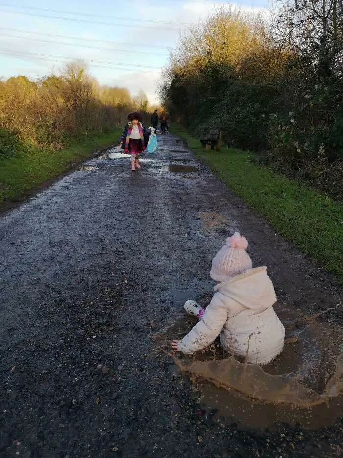 Child in white coat and pink hat splashing in a puddle on a muddy path, capturing a way better photo than expected