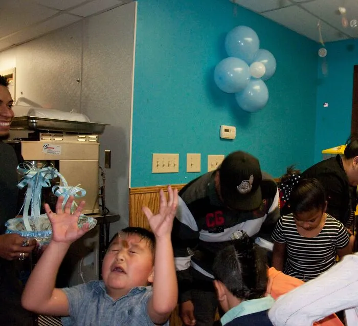 Child making a funny face with hands raised while others in a party setting capture an unexpected better photo.