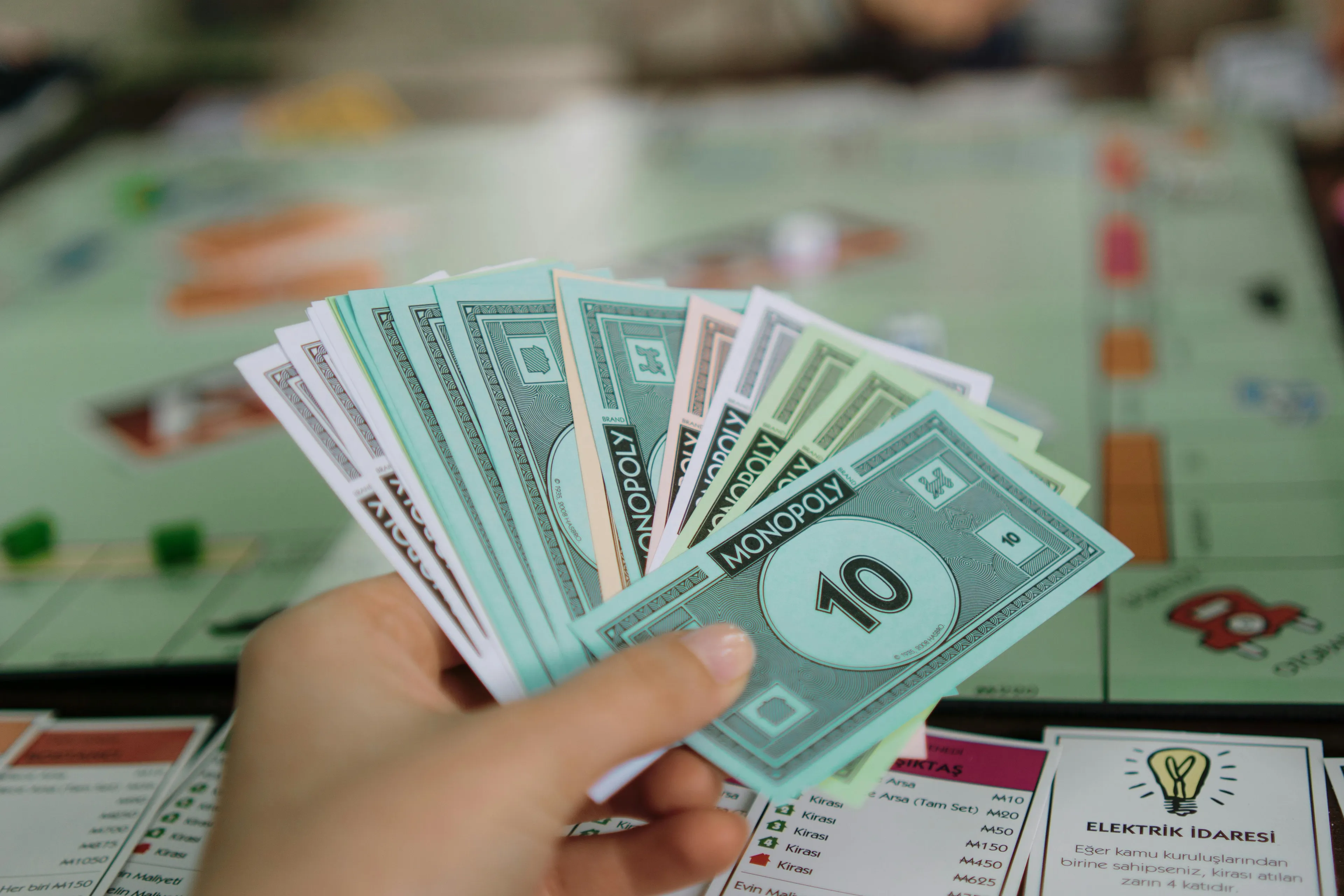 Hand holding Monopoly money with the game board in the background illustrating economics and monopoly concepts.