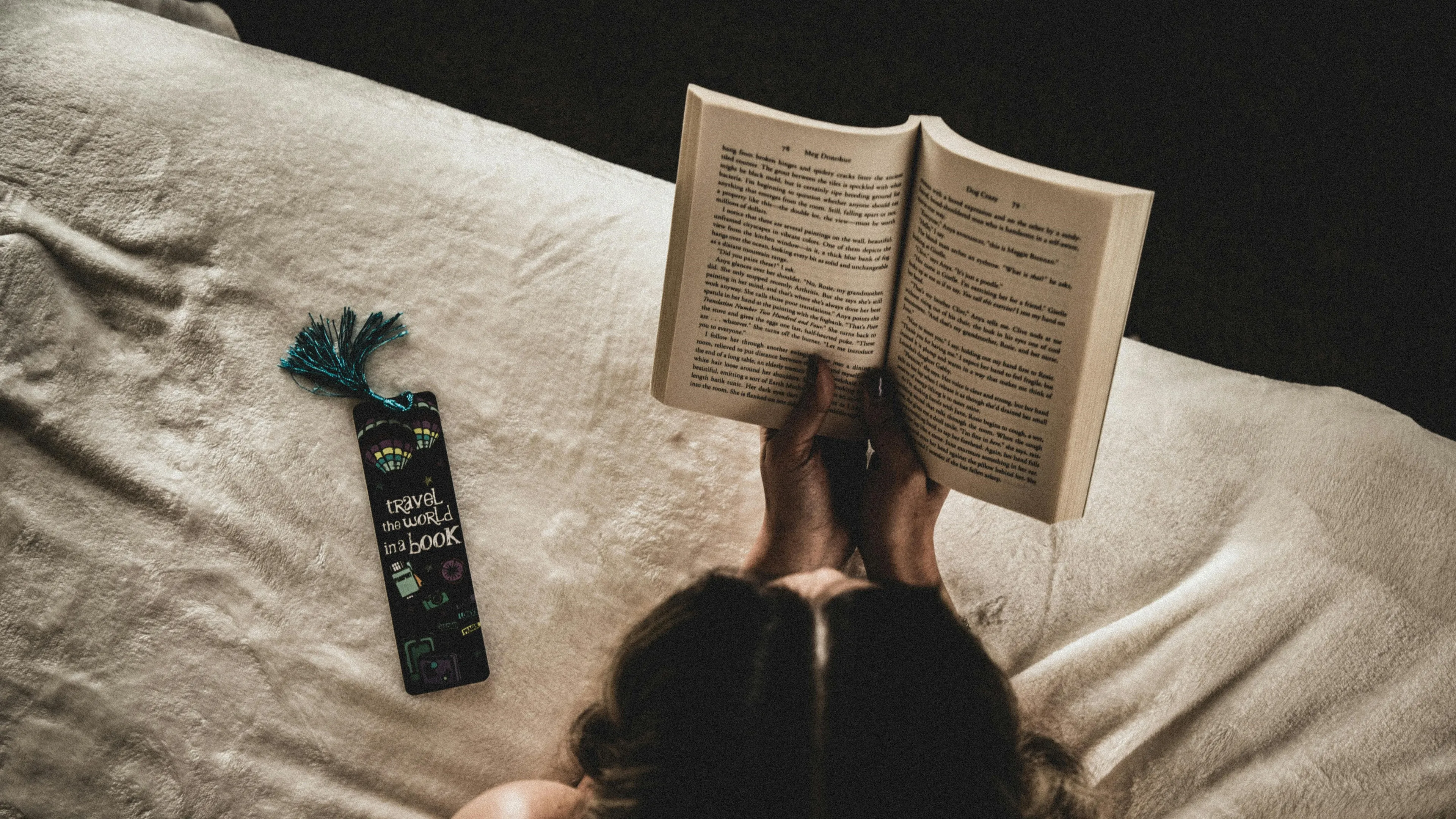 Person reading a book on a soft blanket with a colorful bookmark about travel, illustrating dramatic irony in literature.