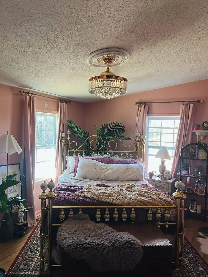 Cozy bedroom with ornate brass bed, layered bedding, plants, patterned rug, and eclectic home decor embracing more is more style.