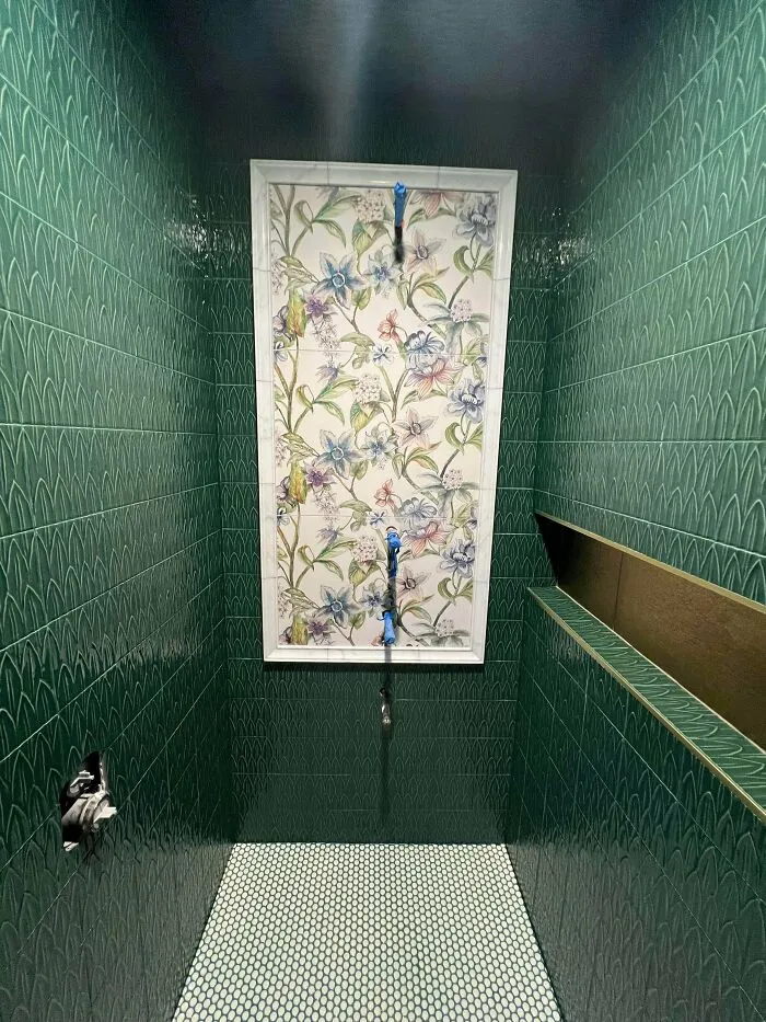 Bathroom shower with green patterned tiles and floral decorative panel, showcasing a more is more home design approach.