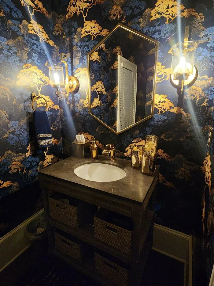 Bathroom with ornate wallpaper, gold accents, and layered decor showcasing more is more home design style.