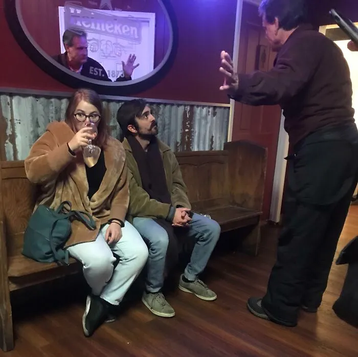 Couple sitting on a bench reacting to a man gesturing, capturing one of the funny photos that say it all instantly.