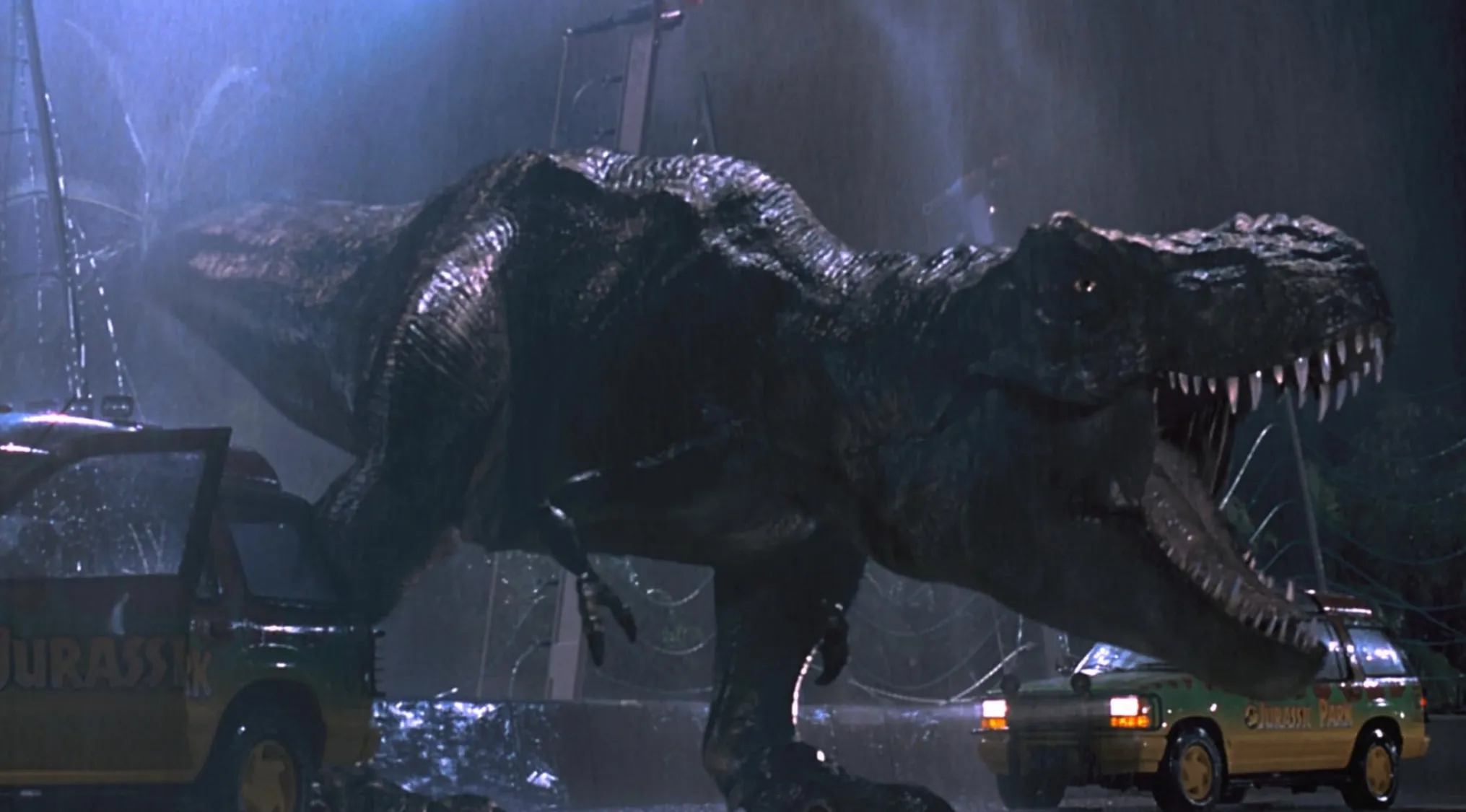 Tyrannosaurus rex roaring beside Jurassic Park tour vehicles in a rainy night scene from the iconic movie tagline quiz.
