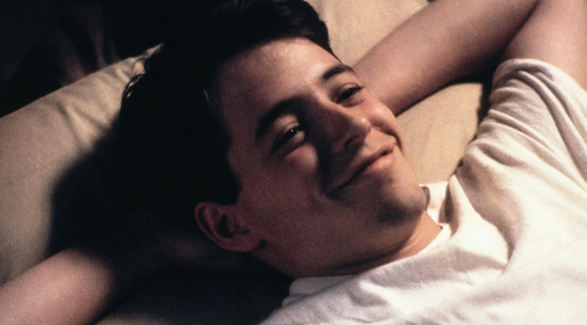 Young man relaxing on bed smiling, related to movie taglines quiz about Ferris Bueller's Day Off film.