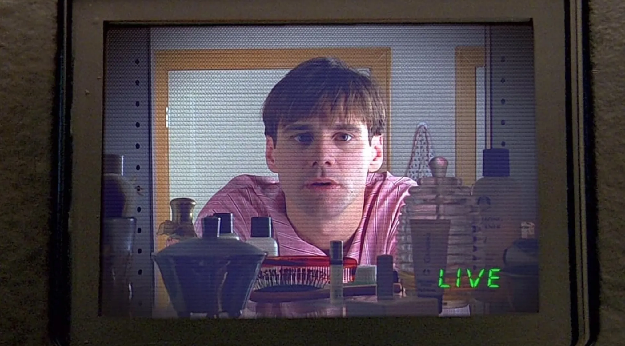 Scene from The Truman Show showing the main character on a live broadcast behind bathroom items on a screen.