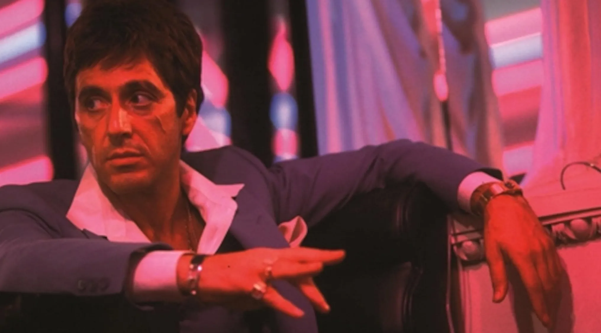 Al Pacino as Tony Montana in Scarface, sitting with a serious expression in a neon-lit room for movie taglines quiz.