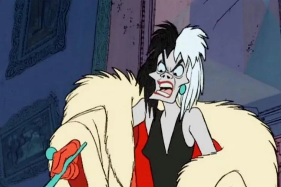 Cruella de Vil with black and white hair wearing a fur coat, angrily pointing inside a dimly lit room.