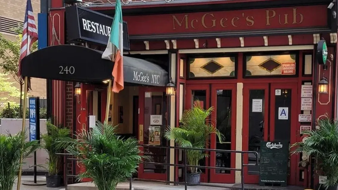 Exterior of McGee’s Pub, a fictional location appearing in Friends, with red facade, black awning, and potted plants outside.