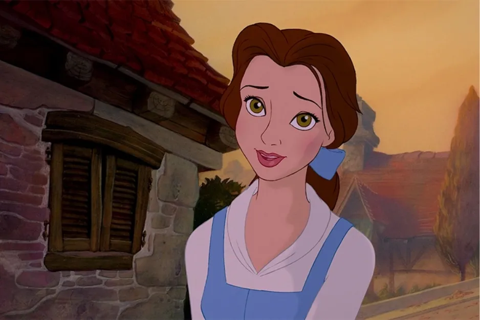 Belle from Disney princess movies with brown hair and blue dress standing outside a village house at sunset.