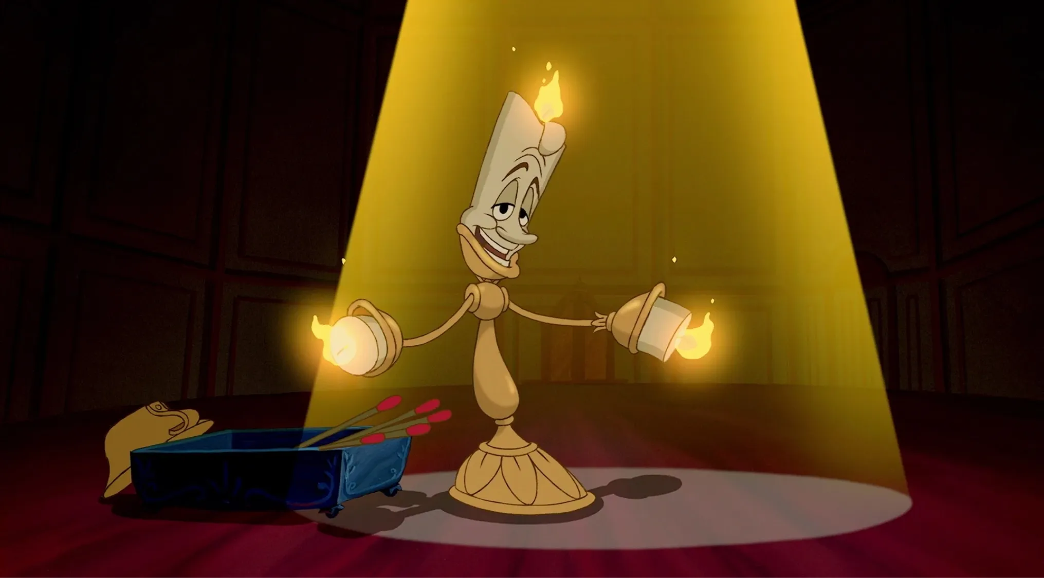 Lumière Disney character standing in a spotlight with lit flames on his arms and head in a dimly lit room.