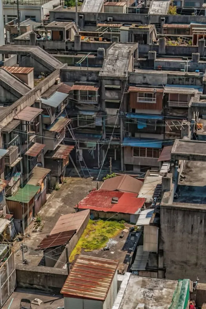 Dystopian urban hell scene showing densely packed, aging buildings with weathered roofs and narrow alleys in modern city life.