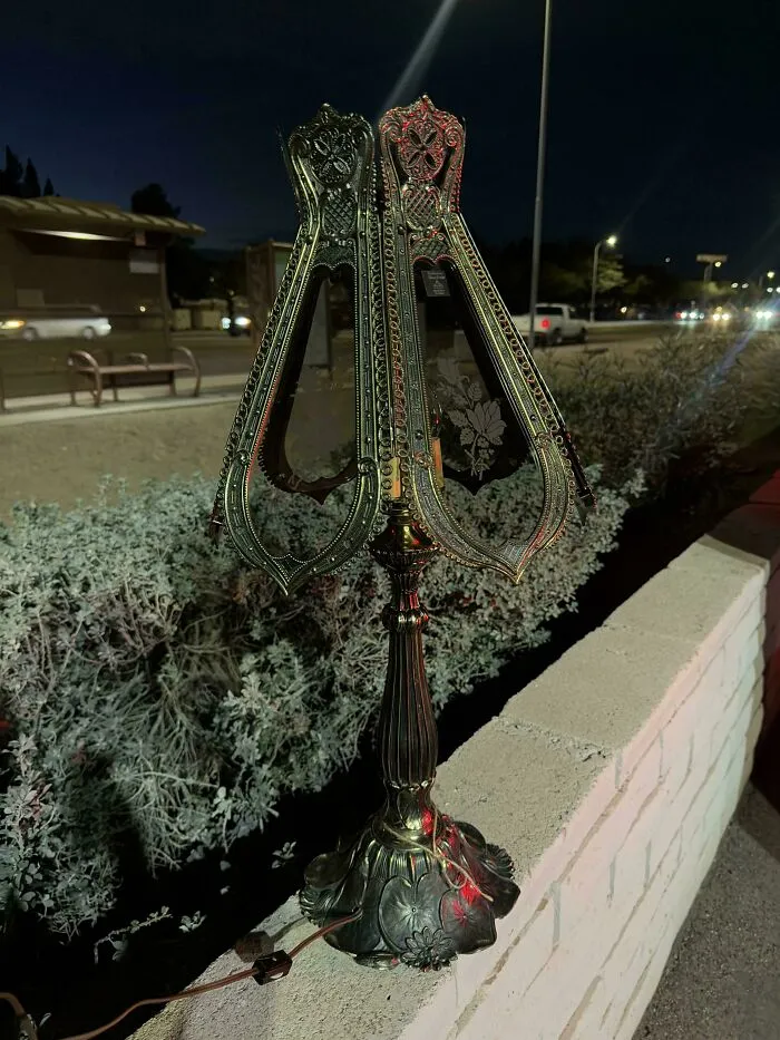 An ornate vintage metal lamp with intricate designs, a jackpot find from a thrift store displayed outdoors at night.