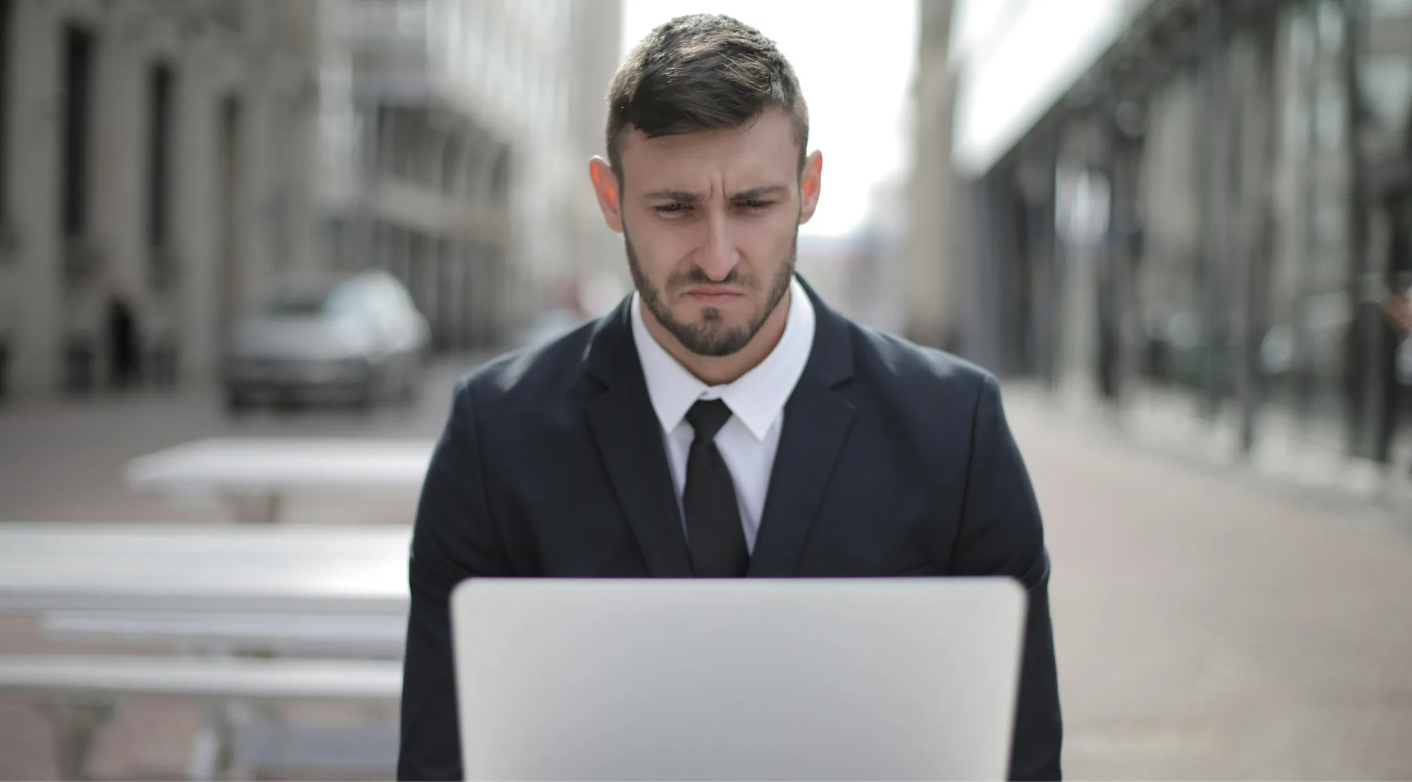 Man in black suit using laptop outdoors, focusing on a difficult general knowledge quiz about Robert Crawley and Violet Crawley.
