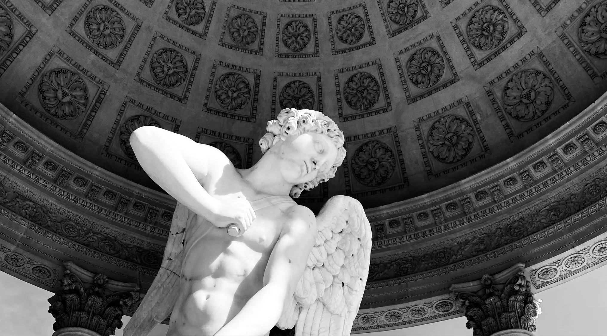 Marble statue of a winged figure beneath an ornate domed ceiling, related to Greek mythology goddess of poetry.