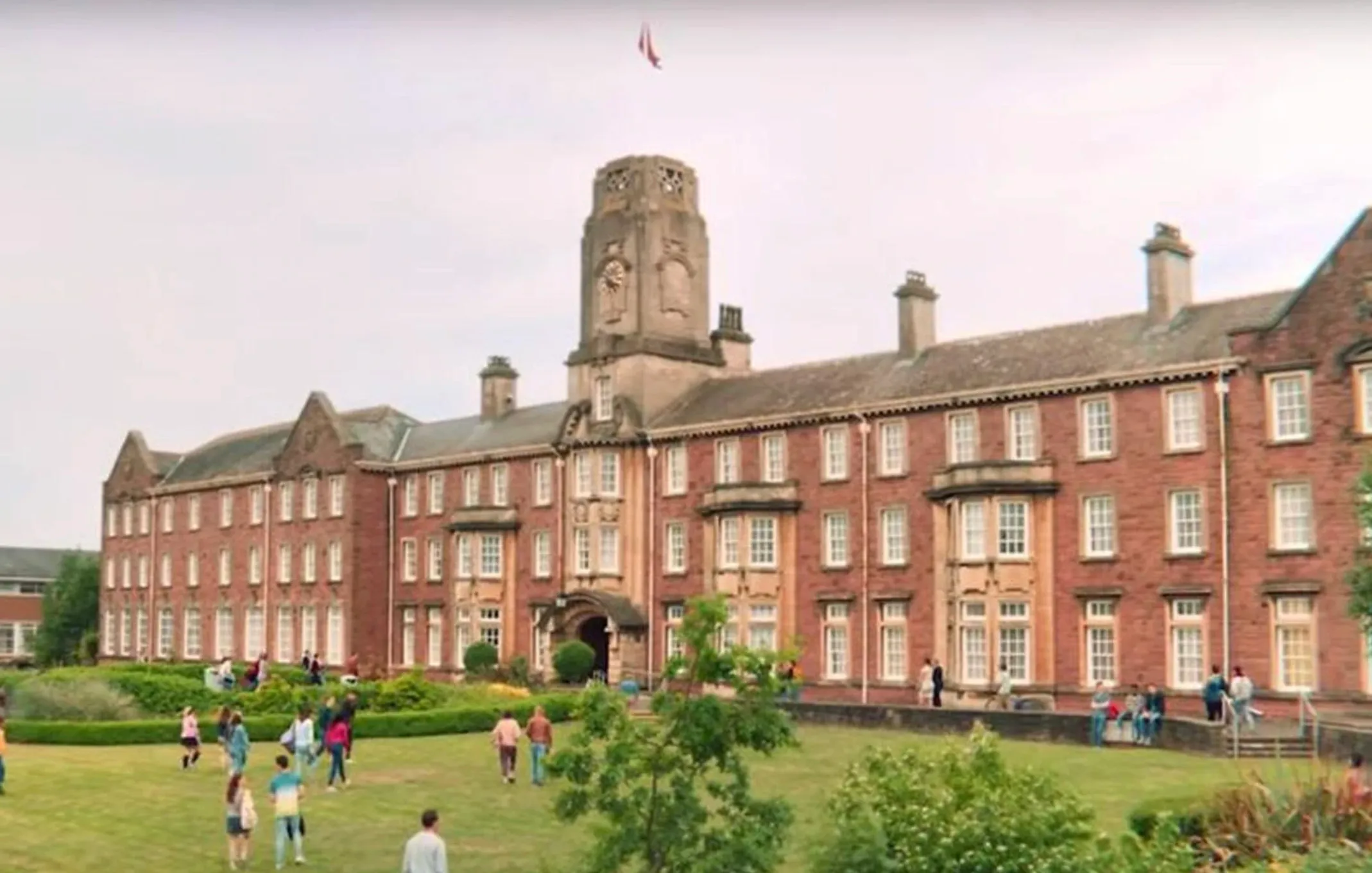 Exterior view of the fictional Moordale school building from the TV series set in Moordale, with people walking nearby.