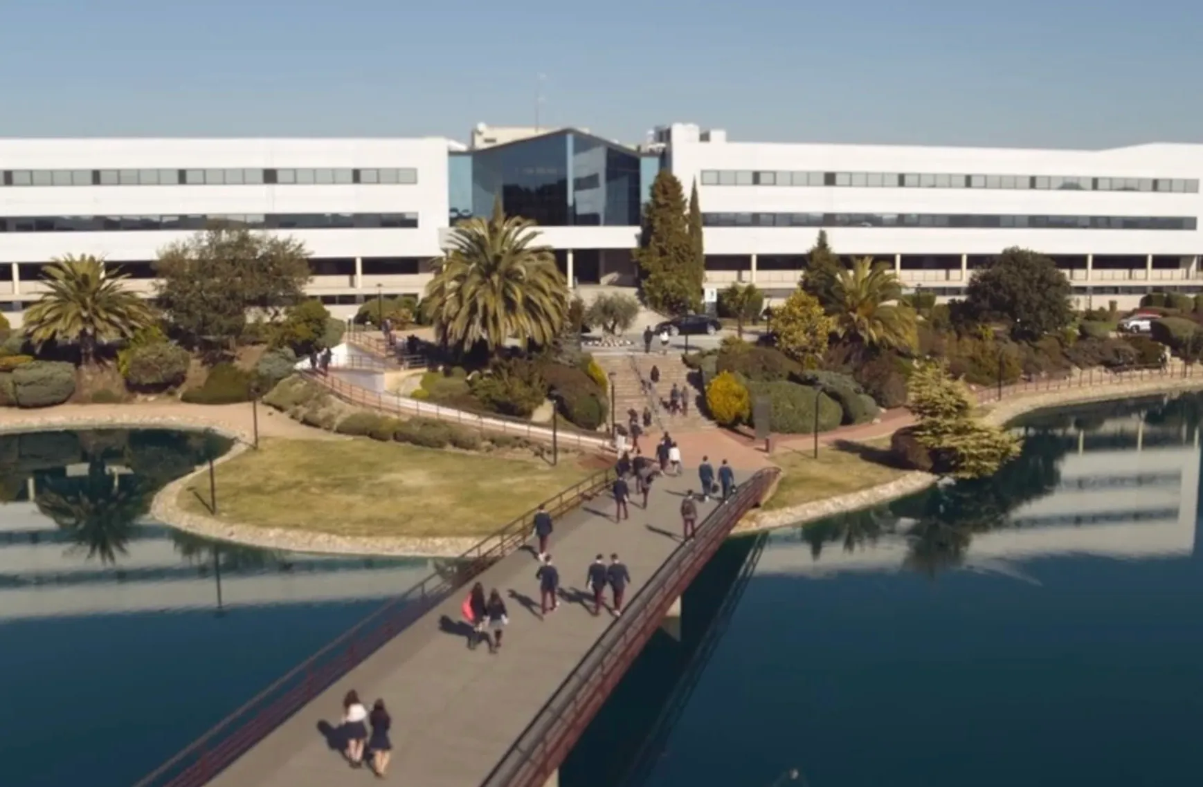 Students walking on a bridge leading to a modern building representing the fictional high school Las Encinas in TV shows.