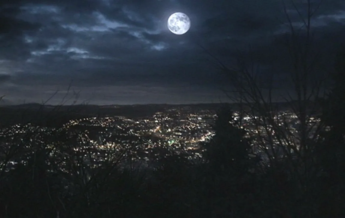 Nighttime view of Beacon Hills city lights under a full moon, a fictional location in popular TV shows.