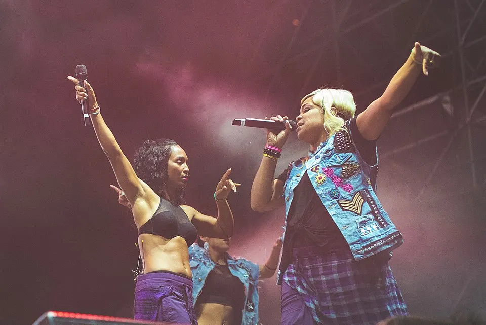 Two female performers on stage singing and dancing, highlighting 1990s hit song by TLC in a colorful concert setting.