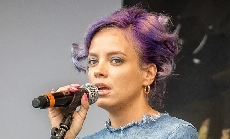 Singer known for hits like Rehab and Back to Black performing with purple hair and gold hoop earrings on stage.