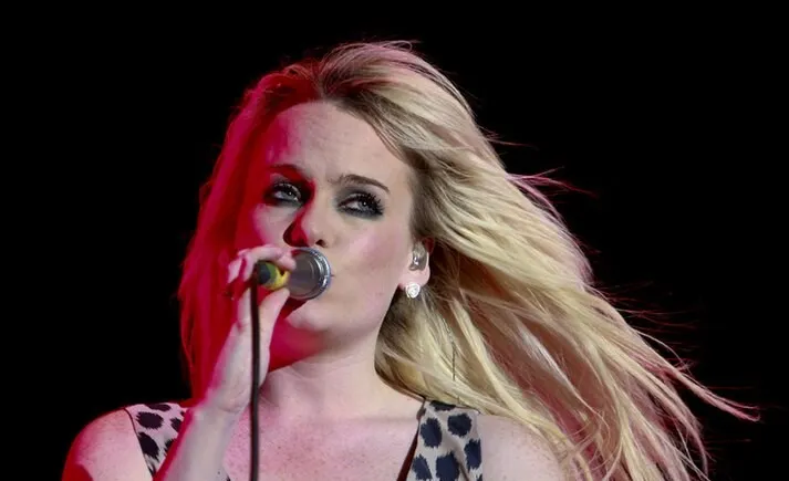 Singer Duffy performing live on stage with blonde hair flowing and holding a microphone during a concert.