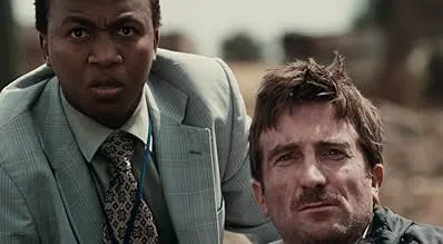 Two men from District 9 film scene, one in suit and the other with dirt on his face, showing intense expressions.