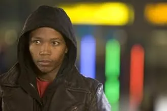 Man wearing a black hoodie and leather jacket in a dimly lit urban setting, representing the film Tsotsi.