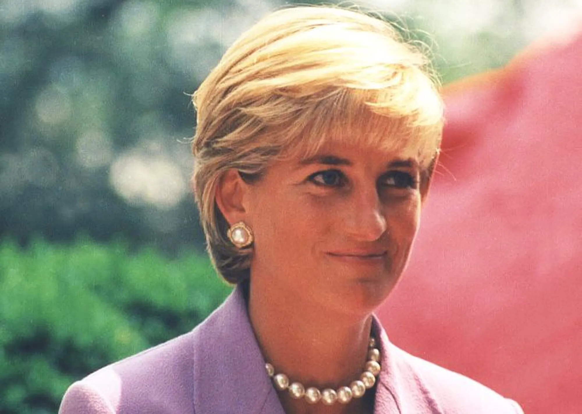 Princess Diana wearing pearls and a lavender suit during her royal tour visit to an African country.