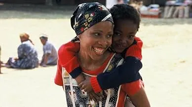 Scene from South African film Yesterday featuring a woman smiling and carrying a child on her back outdoors.