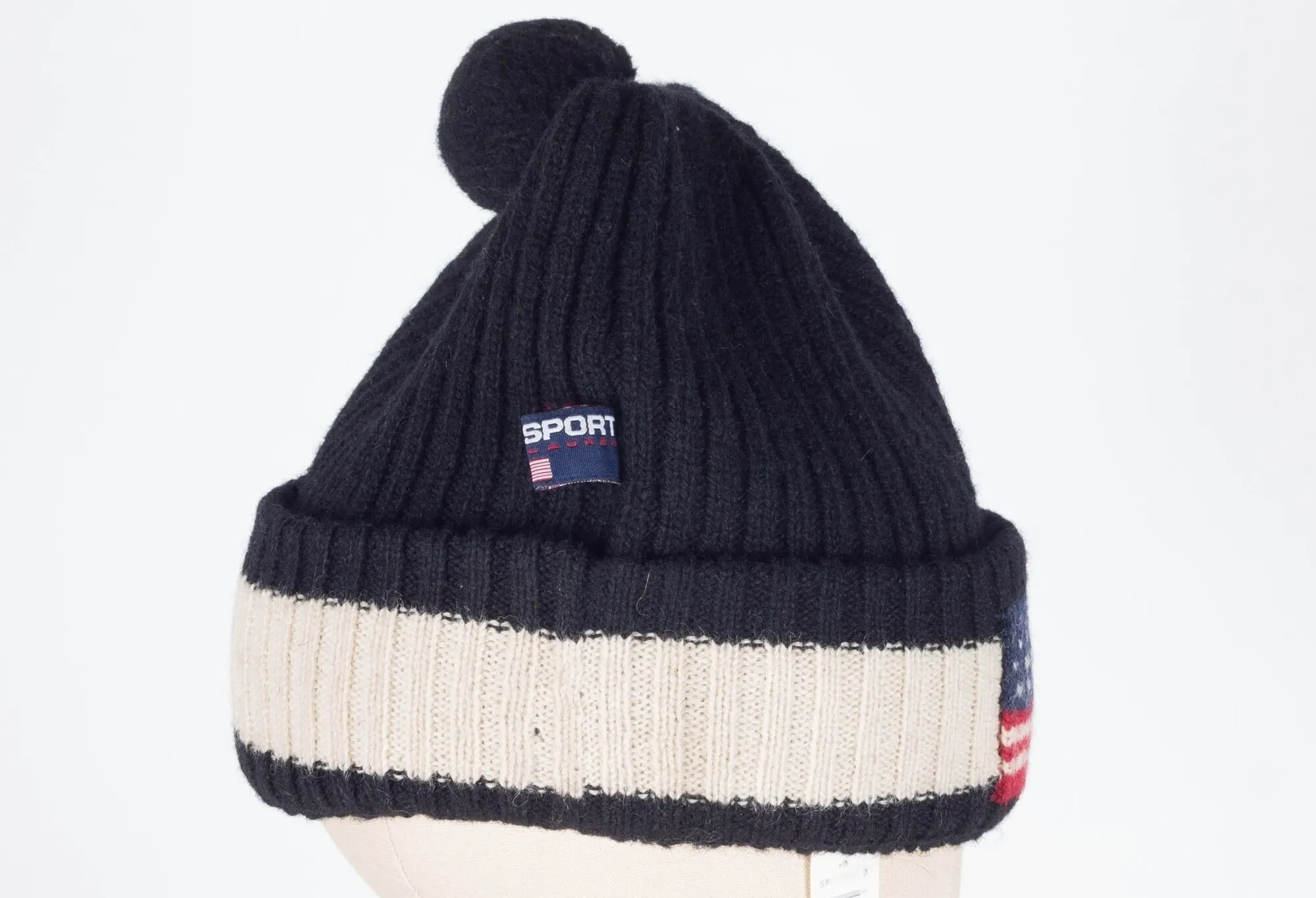 Black and white ribbed knit beanie hat with pom-pom and small patch featuring an American flag design.