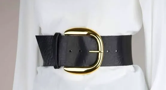 Black oversized belt with a large gold buckle worn around a white blouse, representing 1990s teen pop fashion accessory.