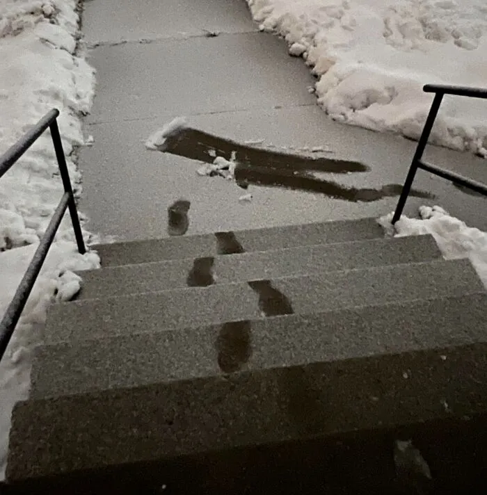 Footprints in the snow showing a funny and confusing path on icy steps and sidewalk in a humorous photo.