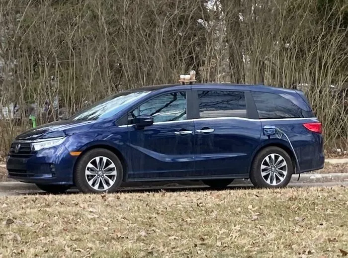 Blue minivan parked by trees with coffee cups on roof, captured in a funny photo that says it all instantly.