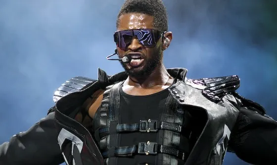 Usher performing on stage wearing futuristic black outfit and sunglasses, known for his 2002 breakup-inspired song Cry Me a River.